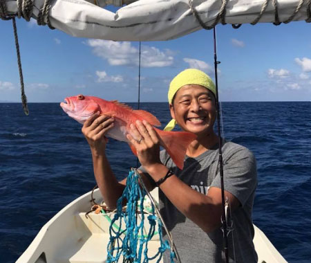 沖縄の海で魚を釣り上げて笑顔を見せる男性