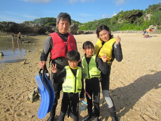 沖縄の青の洞窟近くの浜辺でシュノーケリングツアーに参加する親子