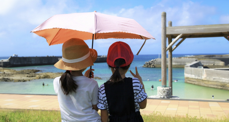 日傘の下で仲良く沖縄の海を見る子供